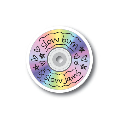 A holographic sticker in the shape of a CD that says Slow Burn and Slow Jams with hearts and stars